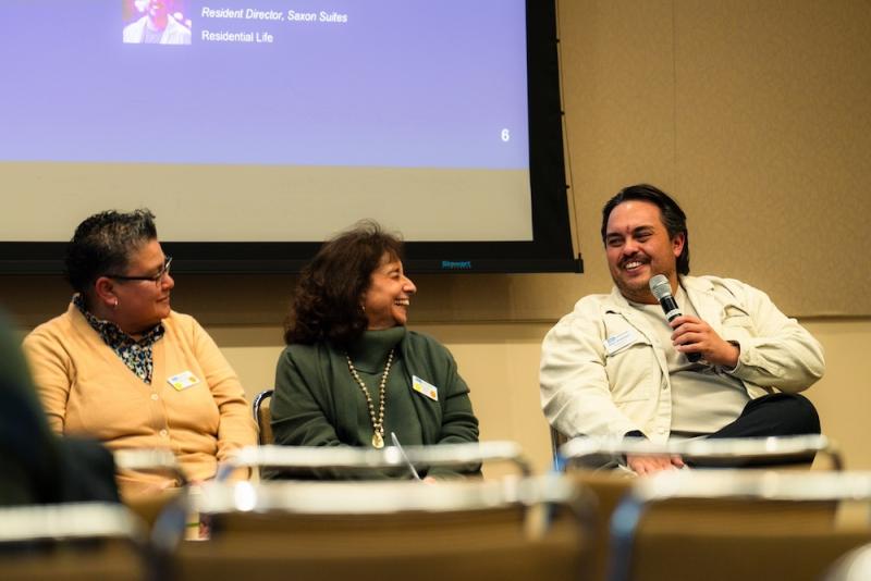 A man talking into a microphone with two women to his left.