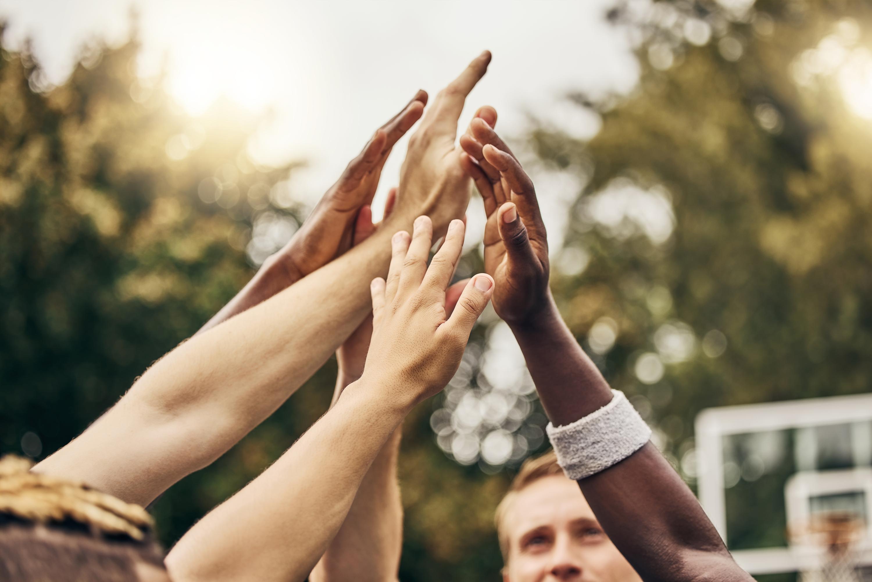 5 people raising their hands together in a team cheer.