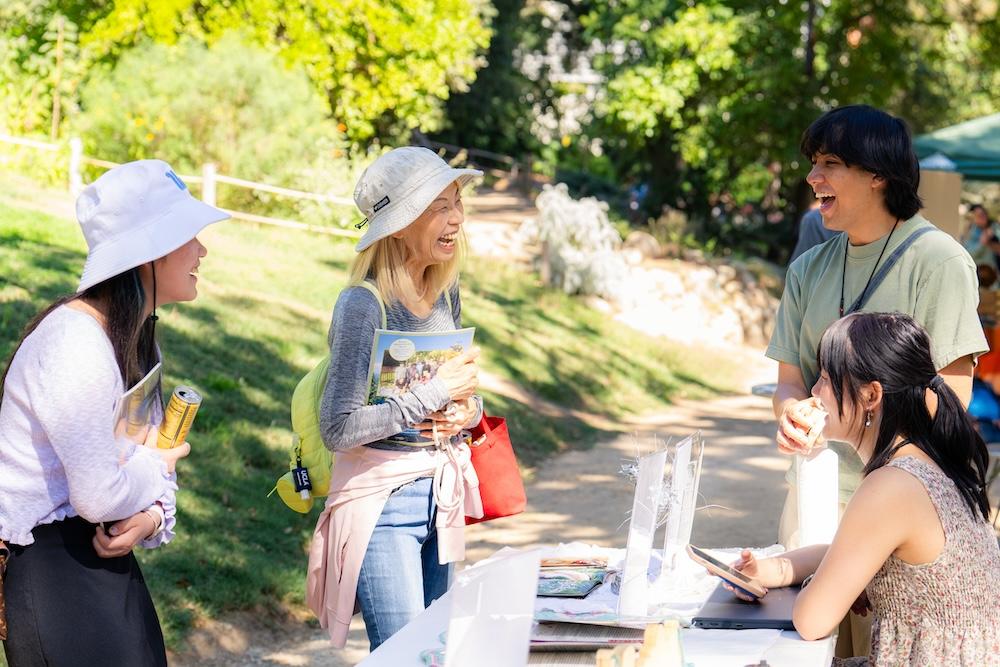 Students smiling and chatting at a booth on a sunny day.