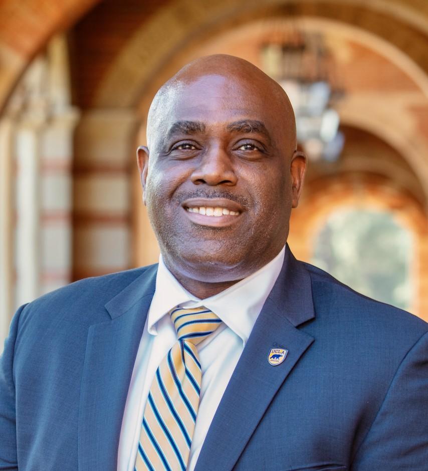 Vice Chancellor Monroe Gorden, Jr. stands in the archway of Royce Hall, wearing a blue suit and UCLA pin