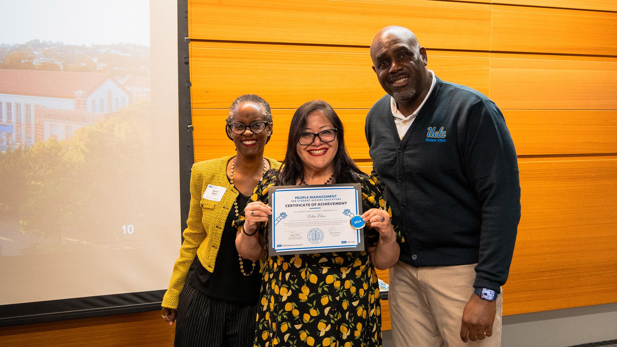 Three people smile proudly. One of them holds a certificate.