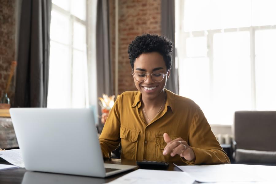 Person smiling in front of laptop while using calculator