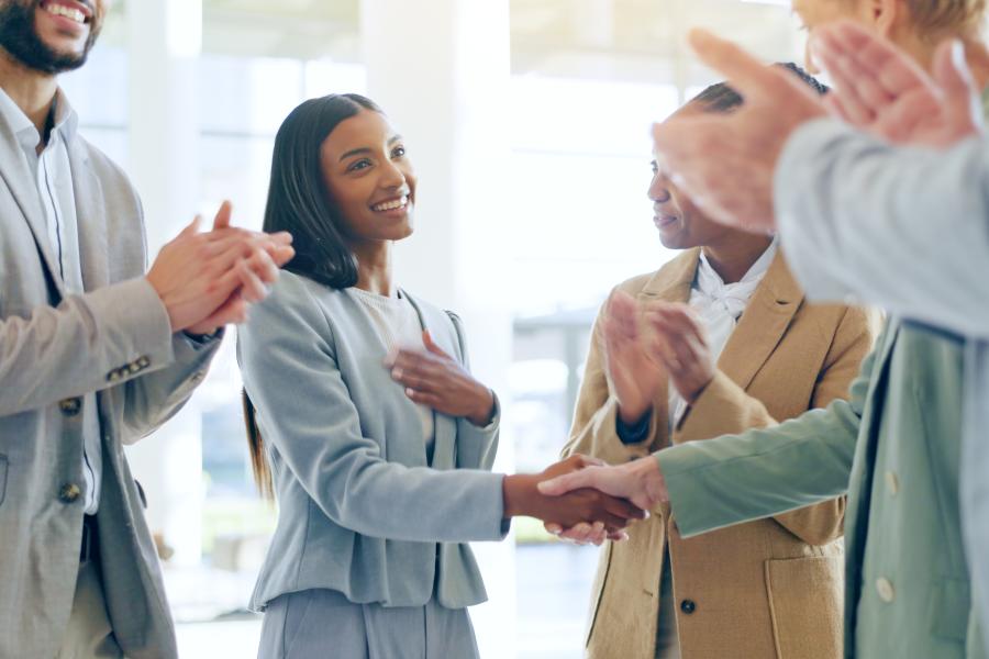 Employees standing in a group clapping and shaking hands with one employee